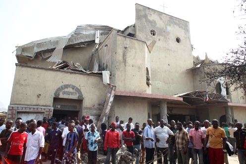 People stand in front of the partially destroyed St Theresa Catholic Church after a bomb blast in the Madala Zuba district of Nigeria's capital Abuja on December 25, 2011. Two explosions near churches during Christmas Day services in Nigeria, including one outside the country's capital, killed at least 28 people amid spiralling violence blamed on an Islamist group. The suspected attacks stoked fear and anger in Africa's most populous nation, which has been hit by scores of bombings and shootings attributed to Islamist group Boko Haram, with authorities seemingly unable to stop them. AFP PHOTO / Sunday Aghaeze