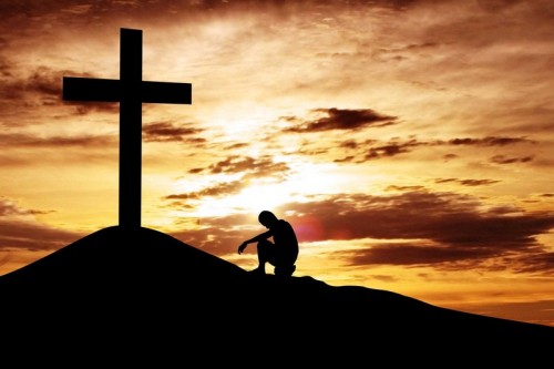 hombre al atardecer orando en una cruz