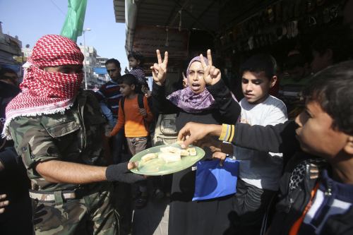 Masked Palestinian distributes sweets as he celebrates with others an attack on a Jerusalem synagogue, in Rafah in the southern Gaza Strip