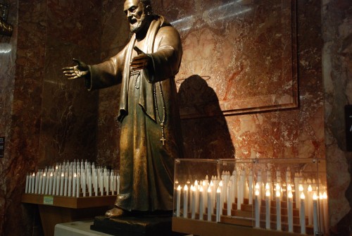 estatua de padre pio con velas fondo